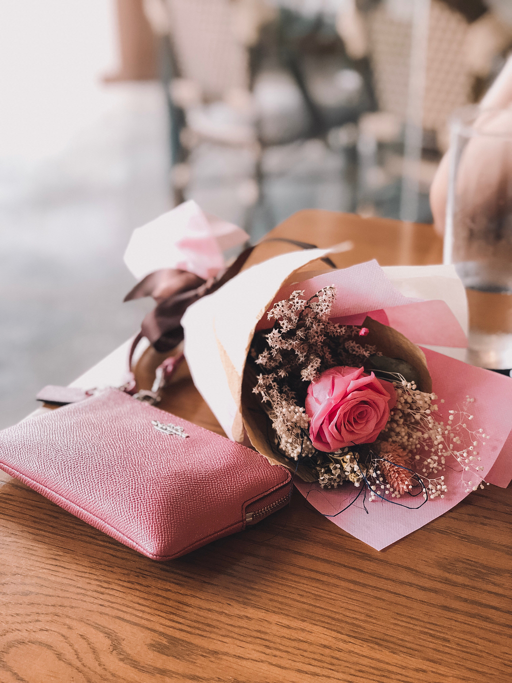 粉红色的玫瑰花附近的粉红色教练皮革钱包在棕色木桌