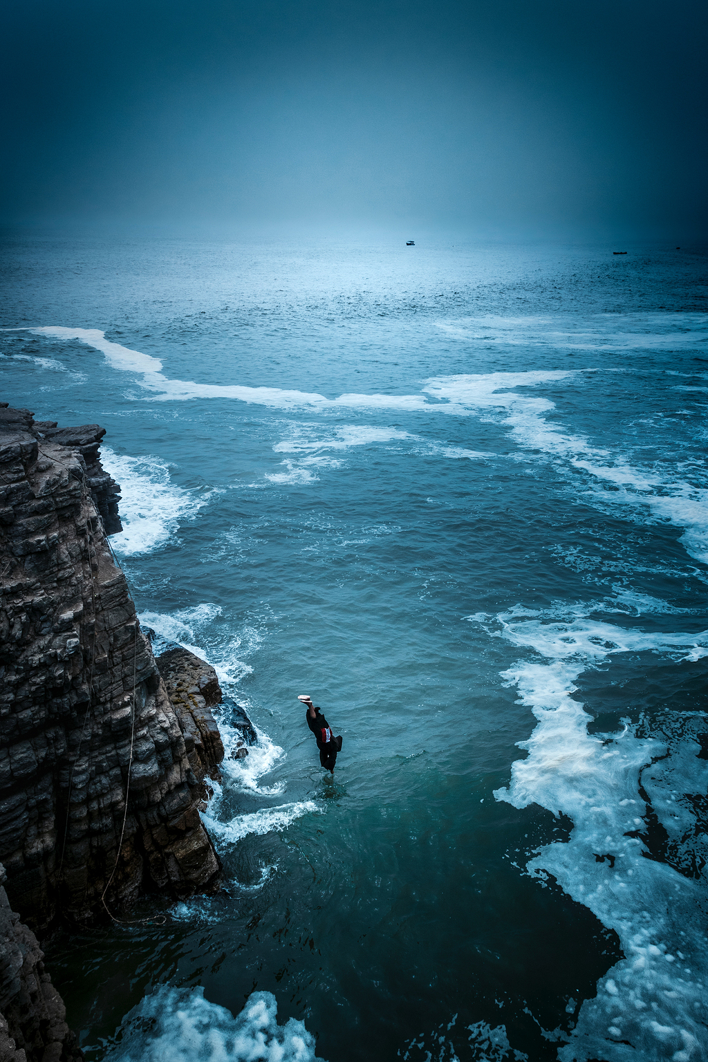 白天从海上岩石悬崖上跳水的人